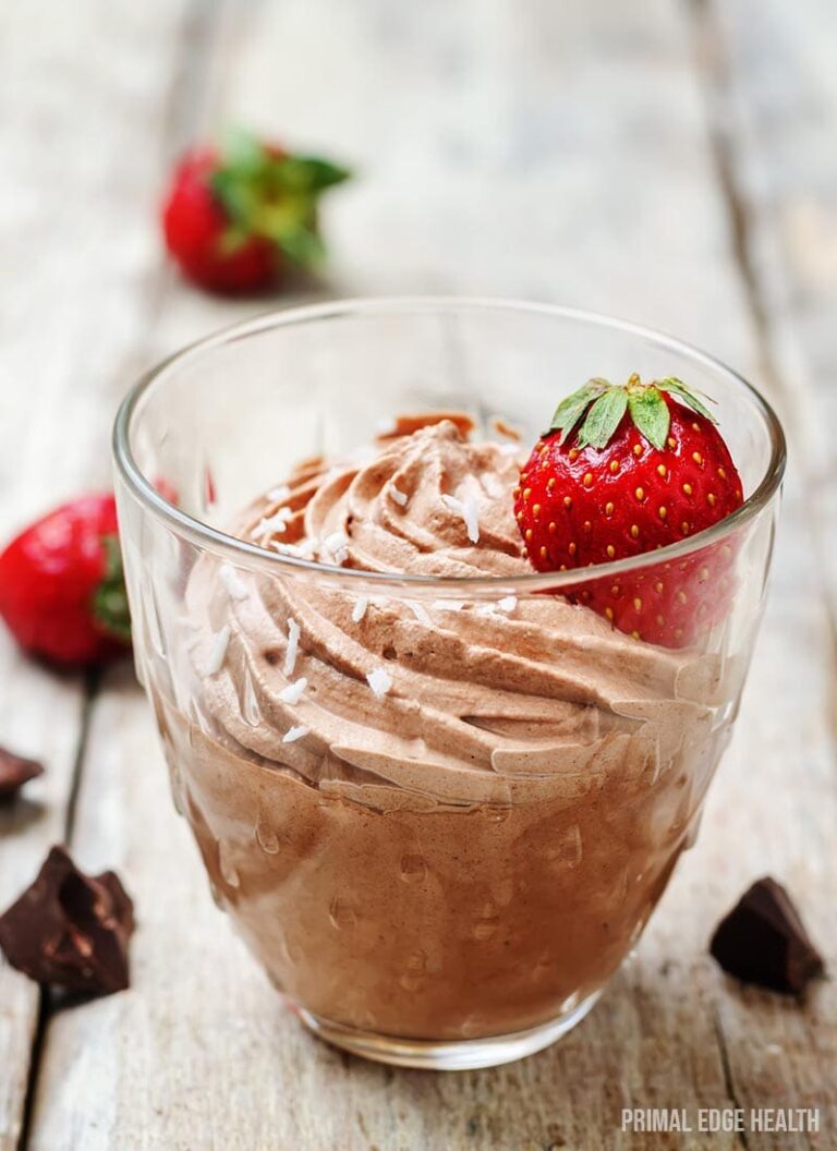 Keto chocolate mousse in a glass with strawberry on a wooden surface.