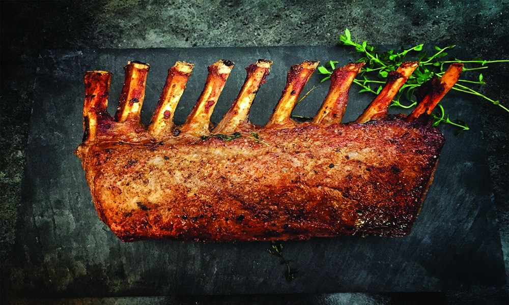 Cooked ribs with stalks of green herb on the side on a black surface.