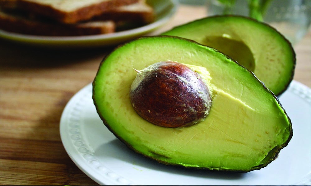 An avocado cut in half on a white plate.