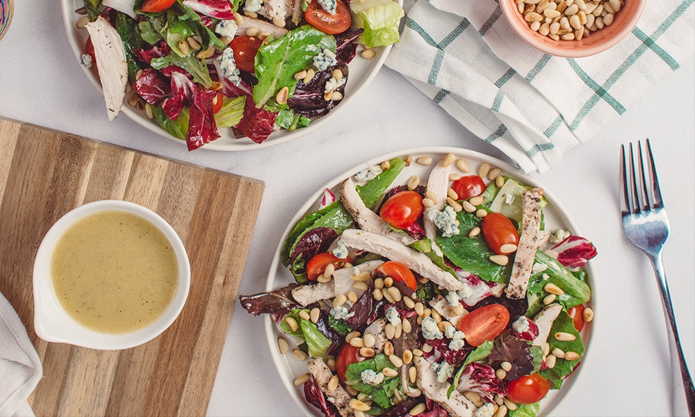 Vegetable salad with stripes of meat next to a small bowl of dressing and s fork.