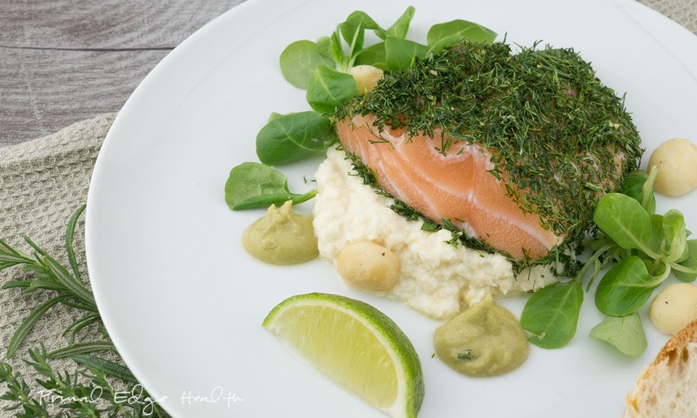 A plate with salmon covered in herbs garnished with more herbs and a slice of lime.