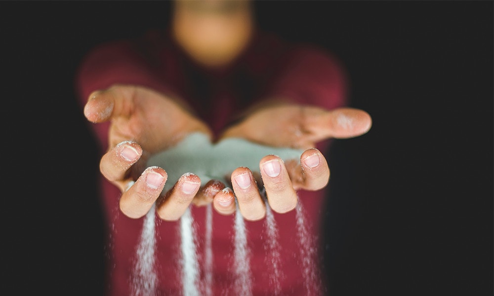 Blue powder spilling out from two hands of a person wearing a red shirt.