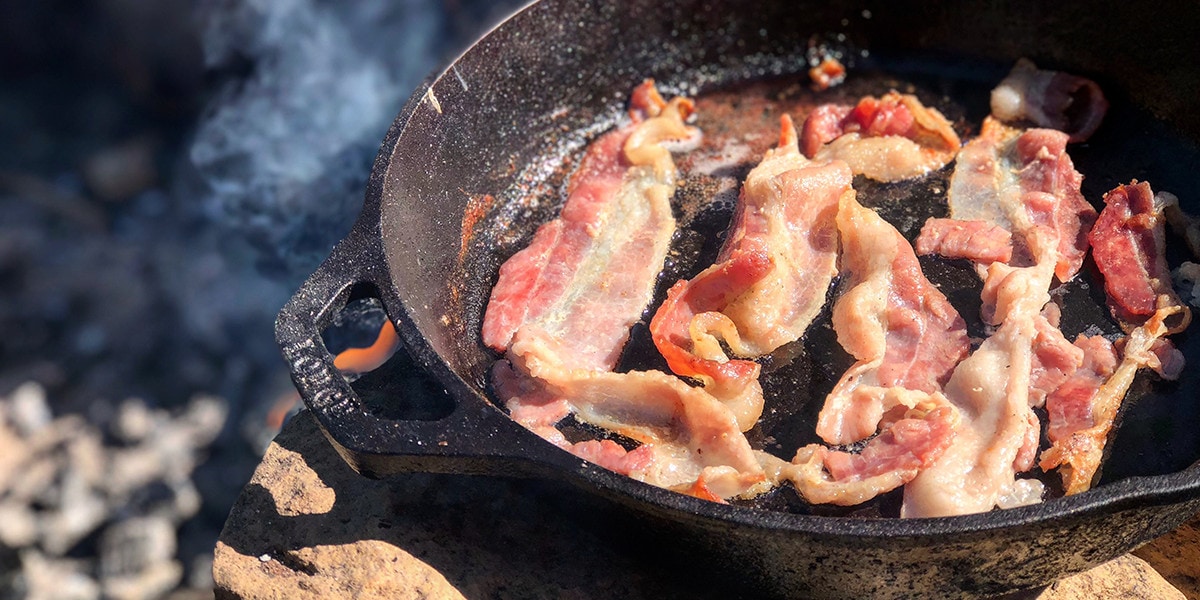 Bacon being cooked in a pan outdoor.