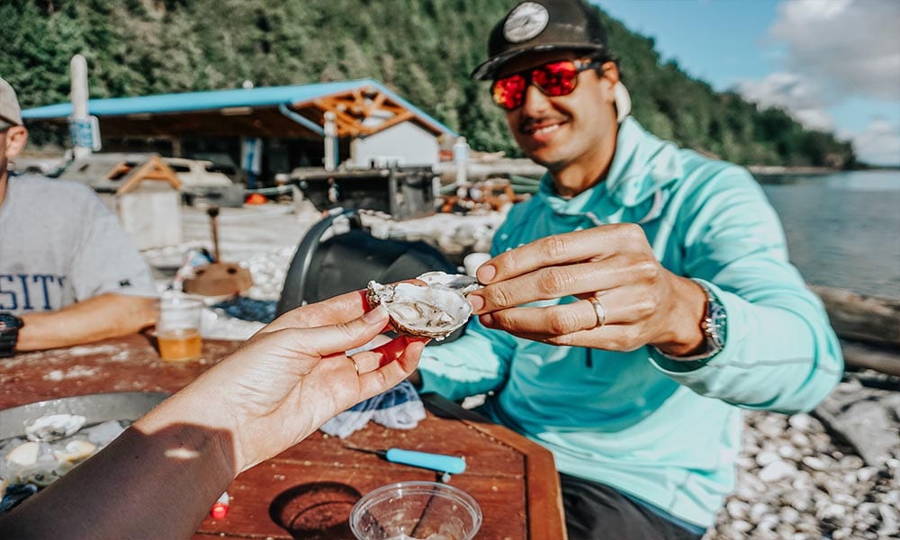 People eating oysters near a body of water.