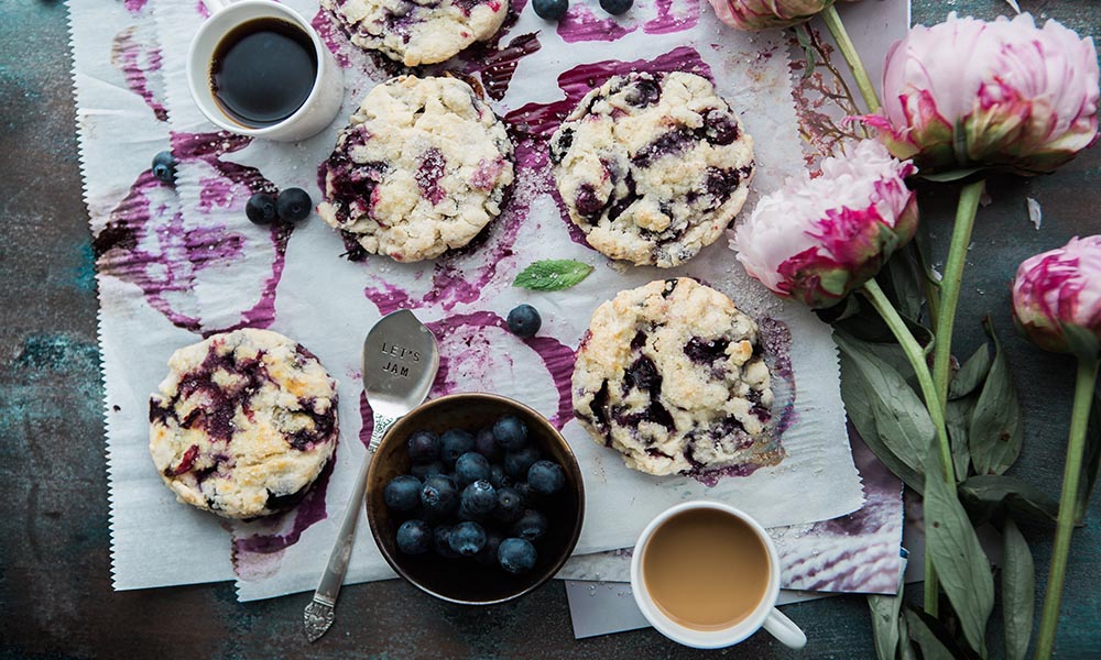 Low-carb blueberry scones next to a cup of coffee and fresh blueberries.