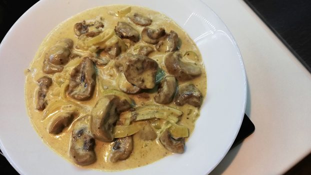 A creamy sauce with mushrooms served on a white plate.