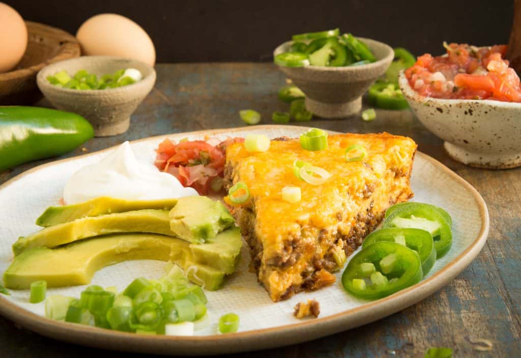 Crustless taco pie in a plate with avocado slices and green pepper.
