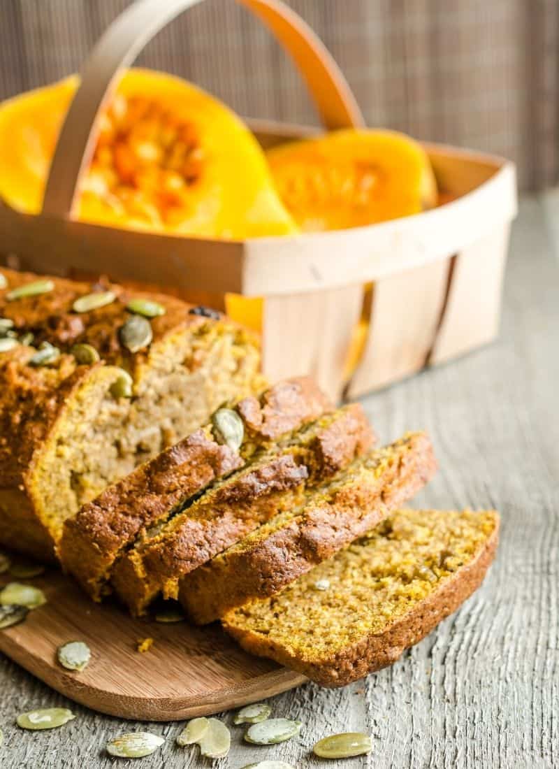 Pumpkin bread on a wooden board with a basket of pumpkin behind.