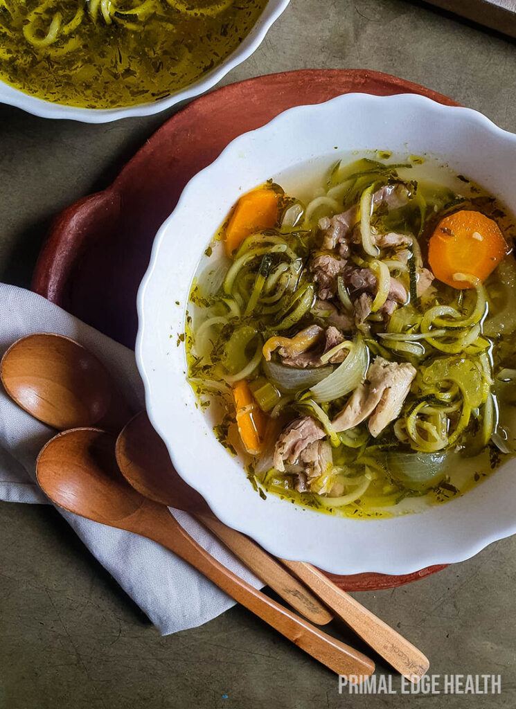 A bowl of keto chicken noodle soup served with wooden spoons.