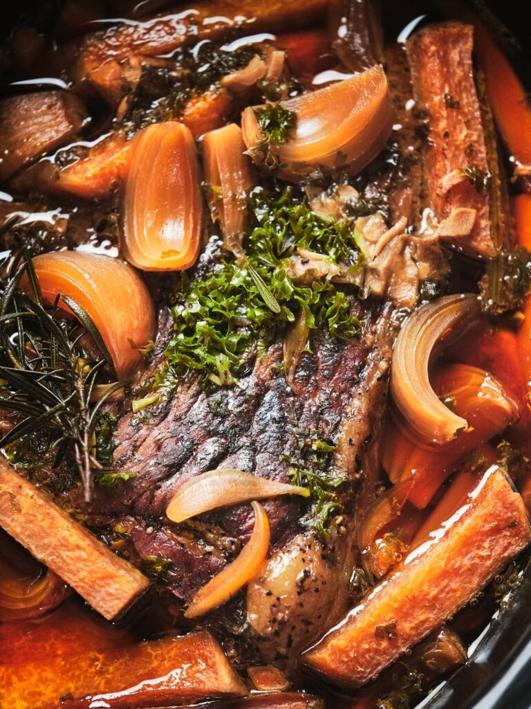 Keto beef roast with carrots, onions, and herbs in a rich sauce, close-up view.