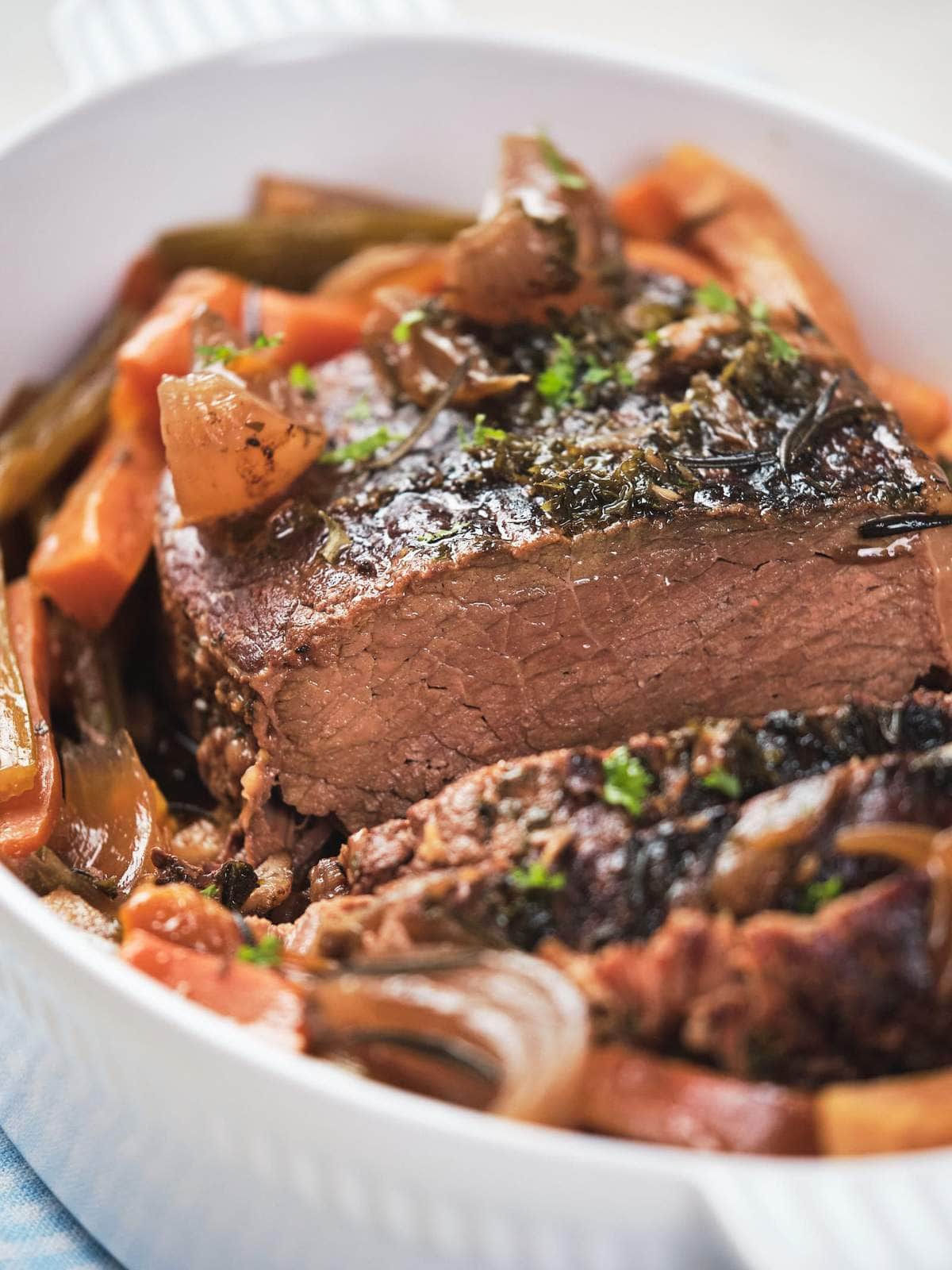A close-up image of a keto beef pot roast with carrots and onions in a white dish.
