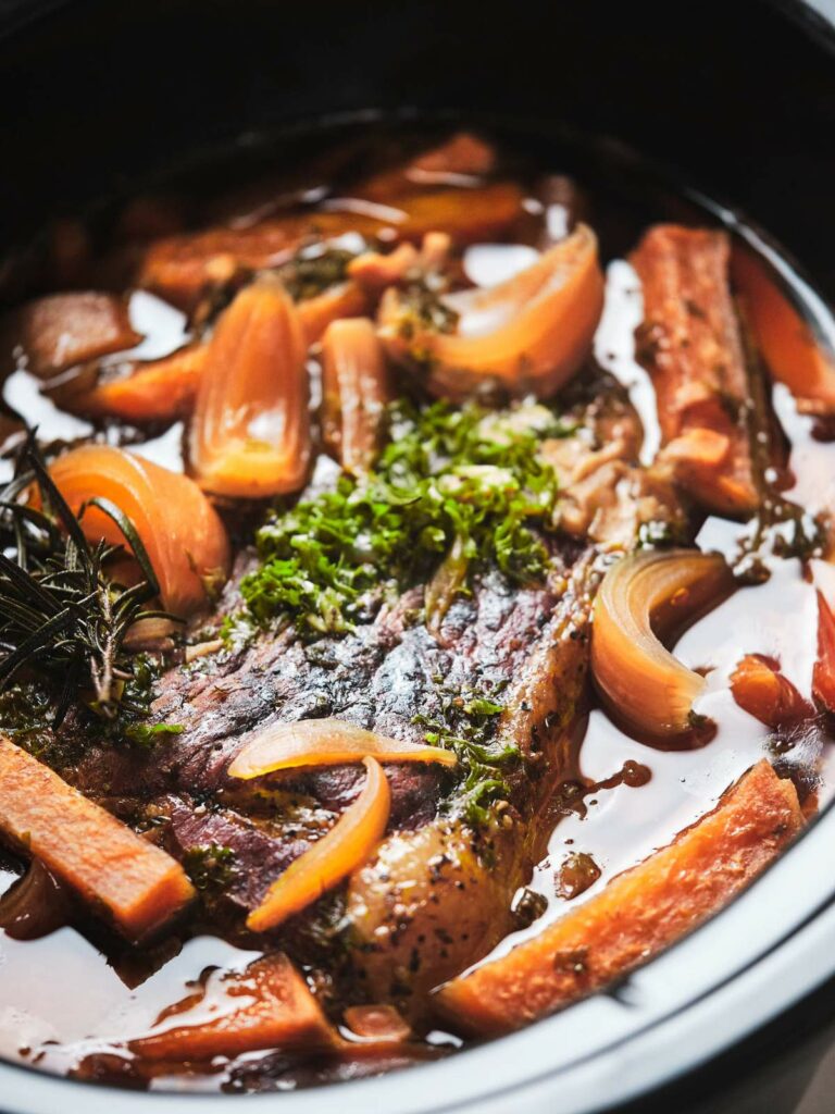 Slow-cooked keto pot roast with carrots and herbs in a black pot.