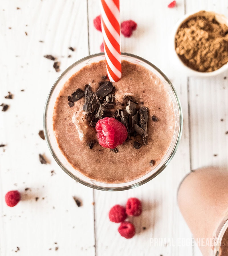Glass of brown smoothie garnished with raspberry and chocolate.