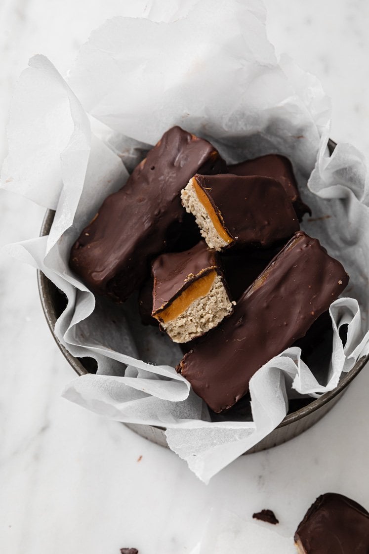 Keto chocolate-covered caramel bars in a bowl with parchment paper.