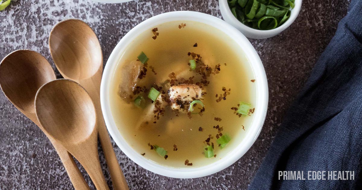 A bowl of broth with herbs and wooden spoons.