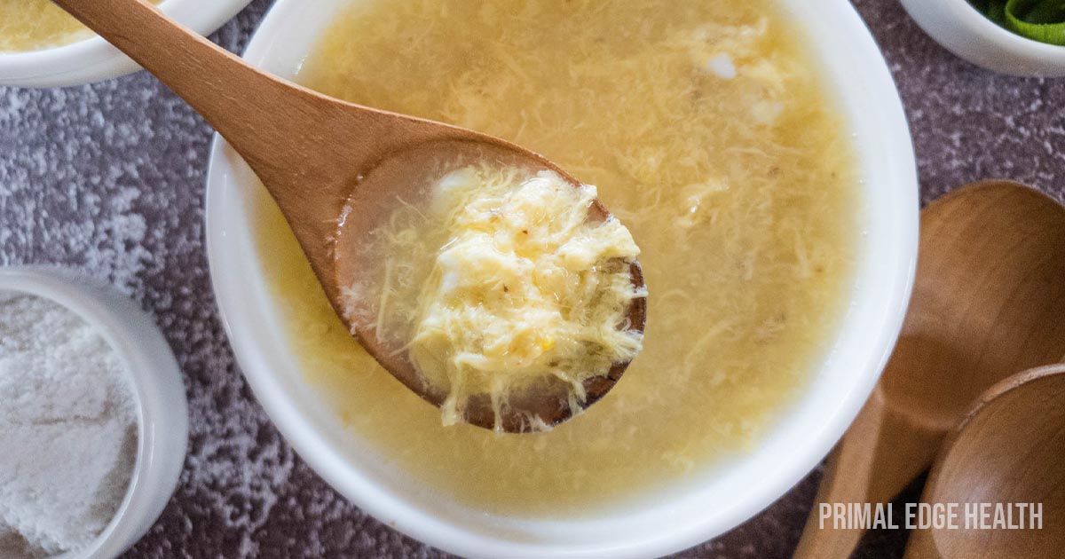 Plain Egg Drop Soup in white bowl with wooden spoon.