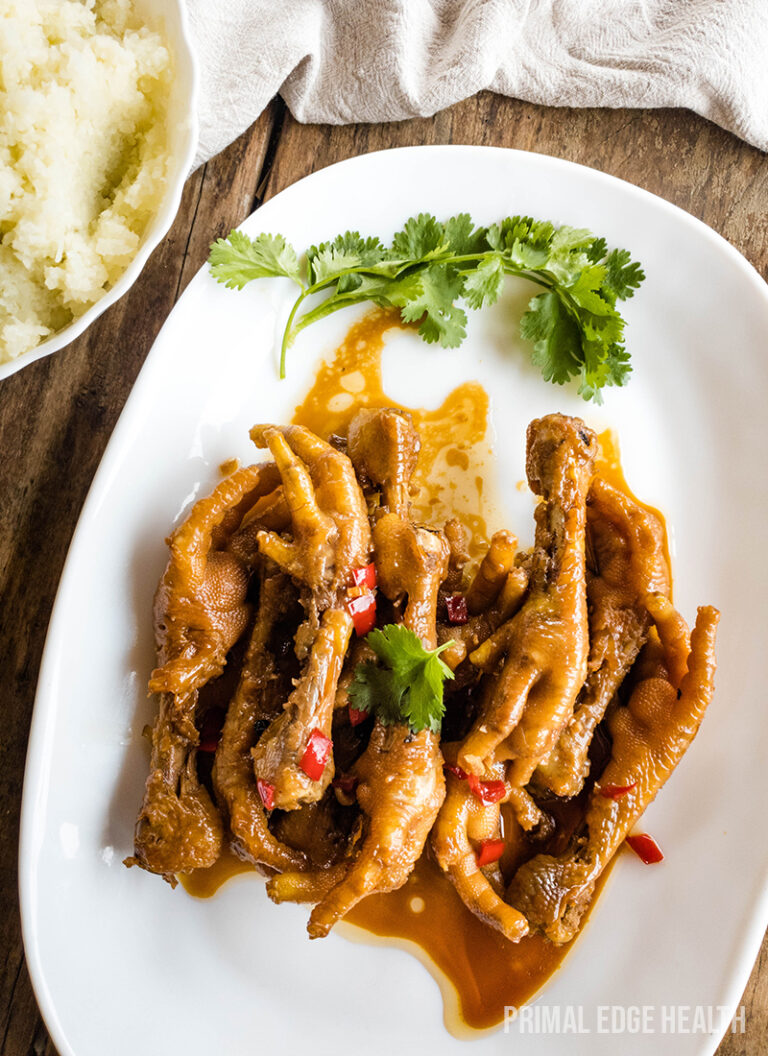 Chicken feet adobo served with garnish on a white place on wooden surface.