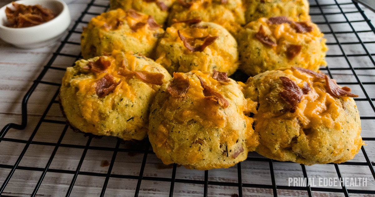 A hand scooping a serving of baked cheesy bread rolls topped with bacon from a rectangular dish.