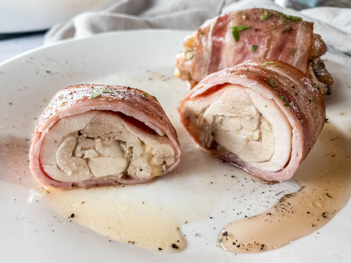 Bacon-wrapped chicken thigh cut in half on a white plate with parsley garnish. 