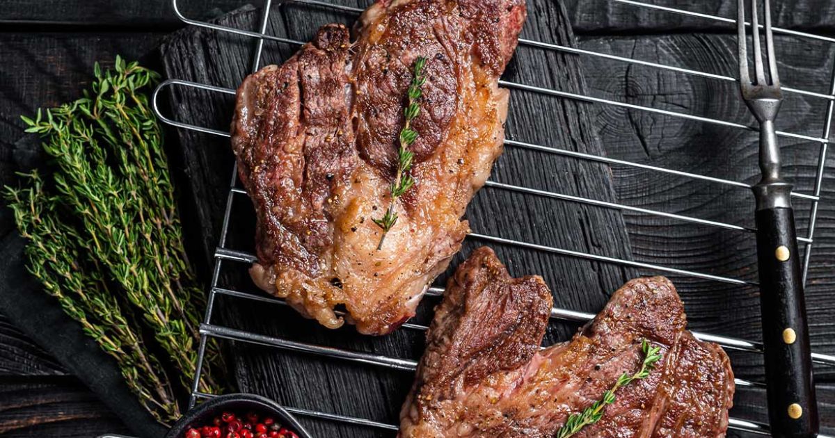 Two steaks on a rack with herbs.