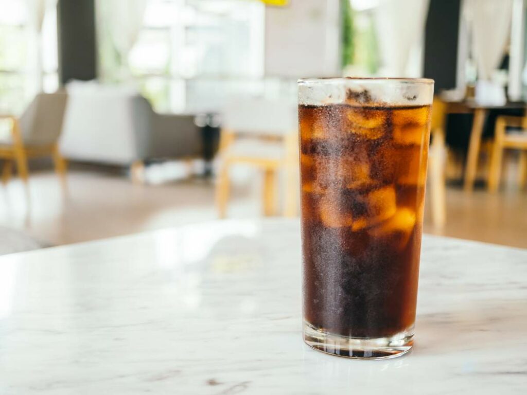 A glass of iced coke on a marble table in a bright, modern cafe setting.