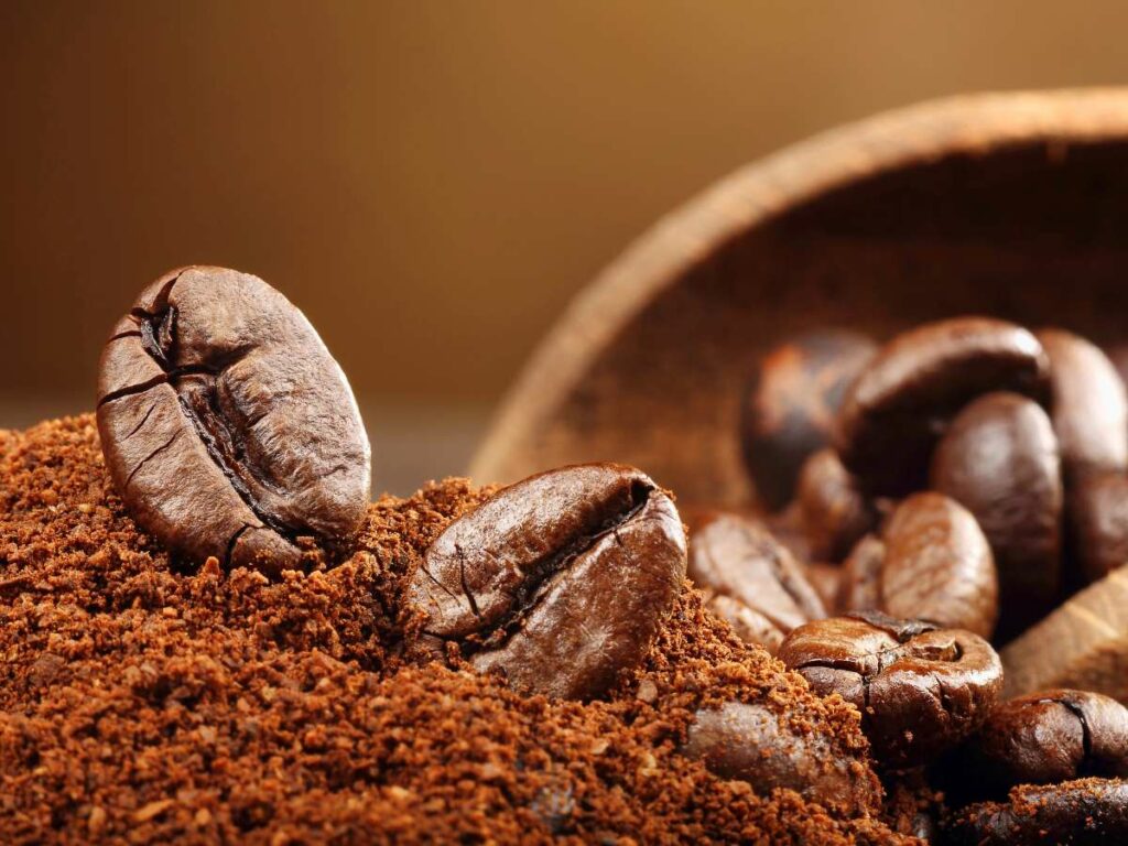 Close-up of roasted coffee beans and ground coffee in a wooden bowl against a warm brown background.
