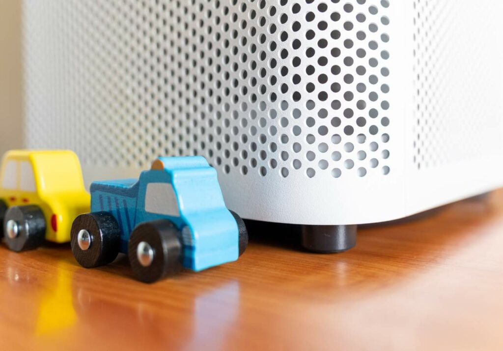 Close-up of two small toy trucks next to the base of a white speaker with a perforated design on a wooden surface.