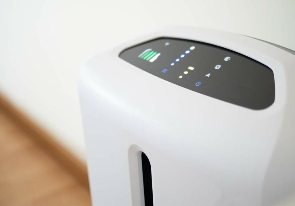 Close-up of a modern air purifier with digital controls displaying power and filter status, situated in a white room.