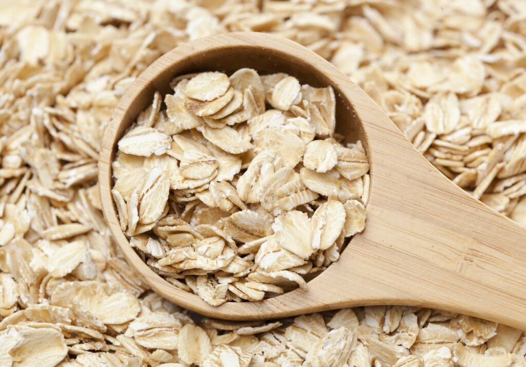 A wooden spoon filled with oat flakes resting on a background of more loose oat flakes.