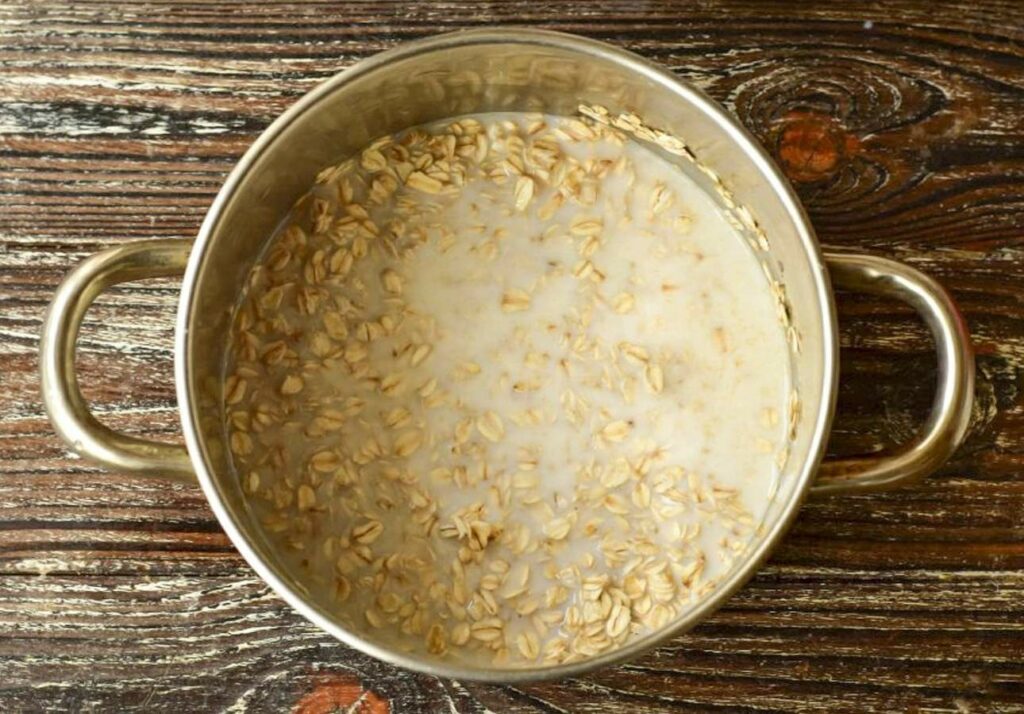 A stainless steel pot containing oatmeal with floating oats, positioned on a wooden surface.