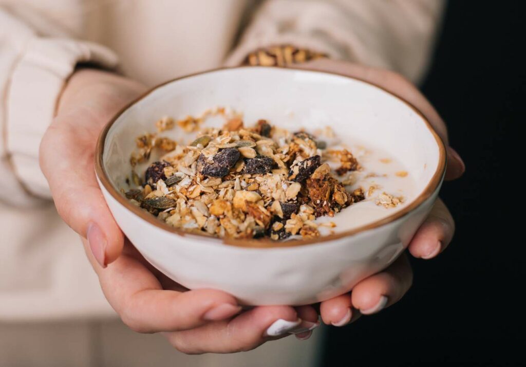 Hands holding a bowl of granola with nuts and dried fruits.