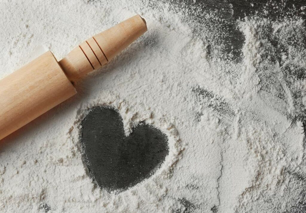 A wooden rolling pin next to a heart-shaped imprint in flour on a surface.