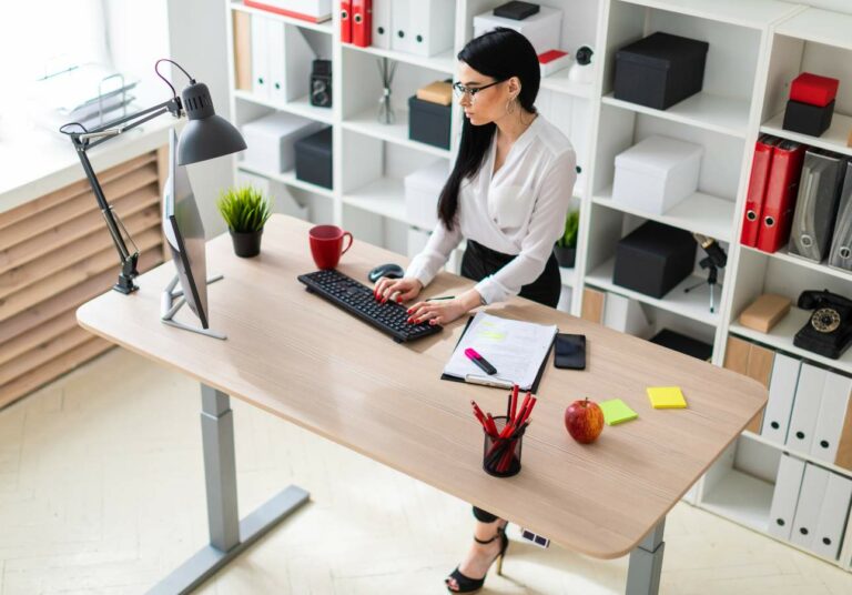 A woman stands at a desk working on a computer.