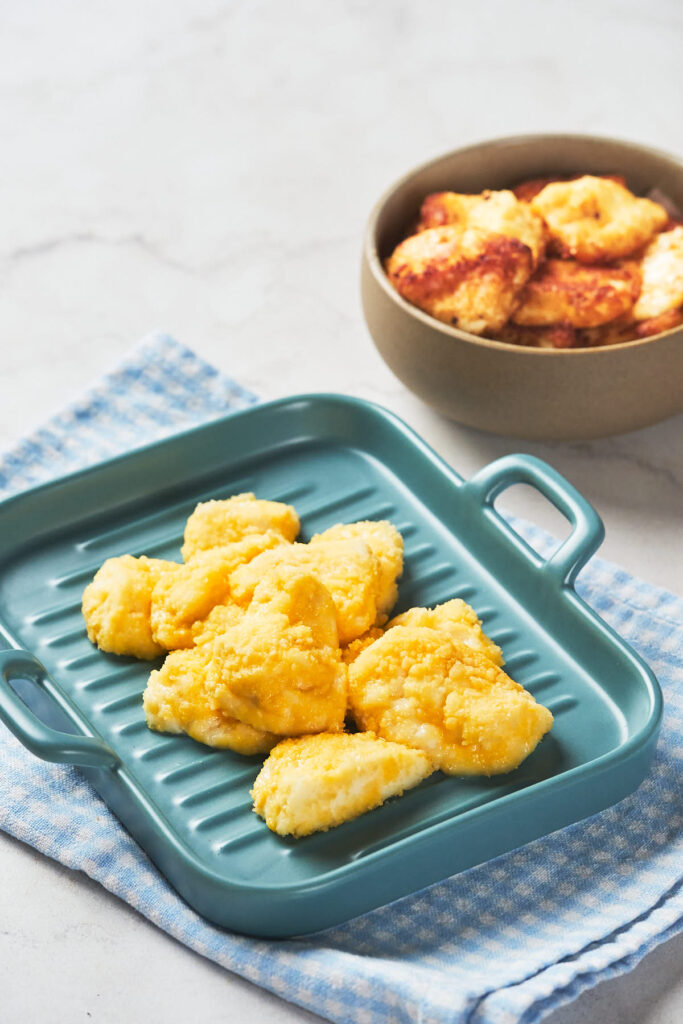 Six pieces of cooked cheese curds are arranged on a blue tray with handles.
