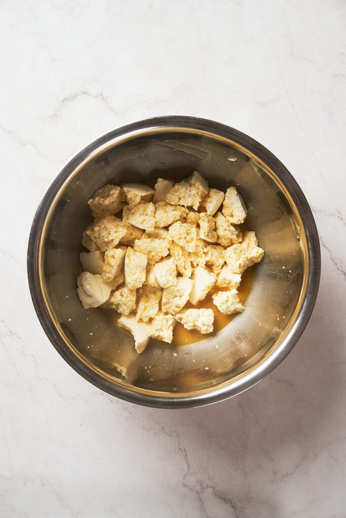A stainless steel bowl containing chunks of crumbled cheese set on a white marble surface.