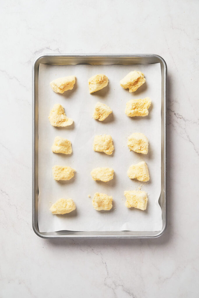 A baking tray lined with parchment paper holds evenly spaced cheese curds.