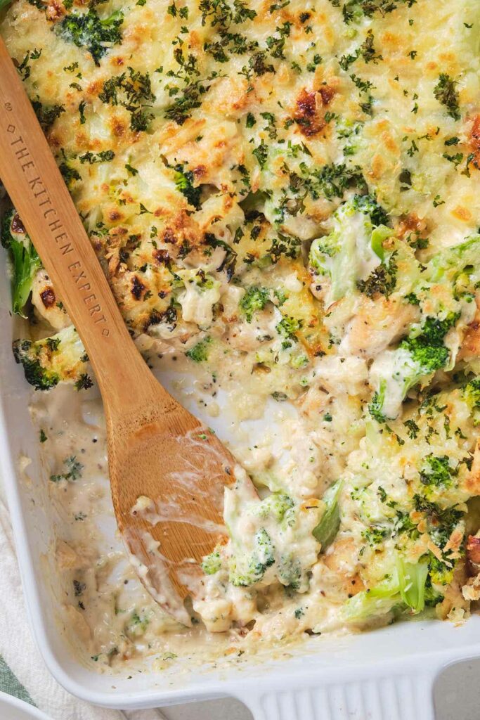 Close-up of a baked broccoli and cheese casserole in a white dish with a wooden spoon.