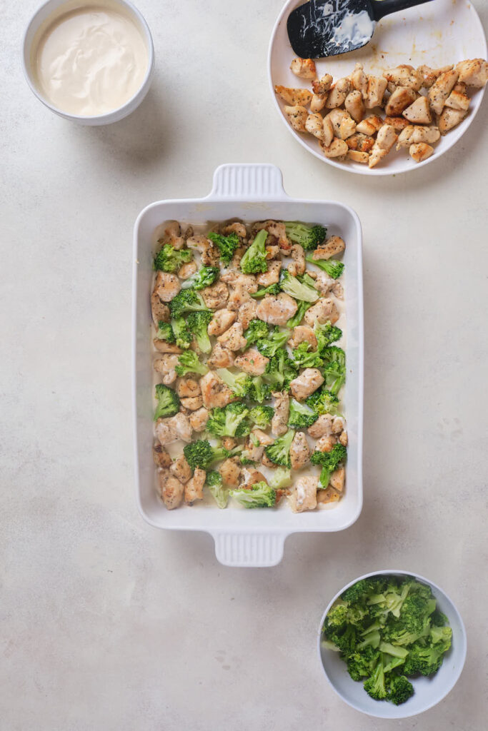 A white casserole dish filled with cooked chicken pieces and broccoli.