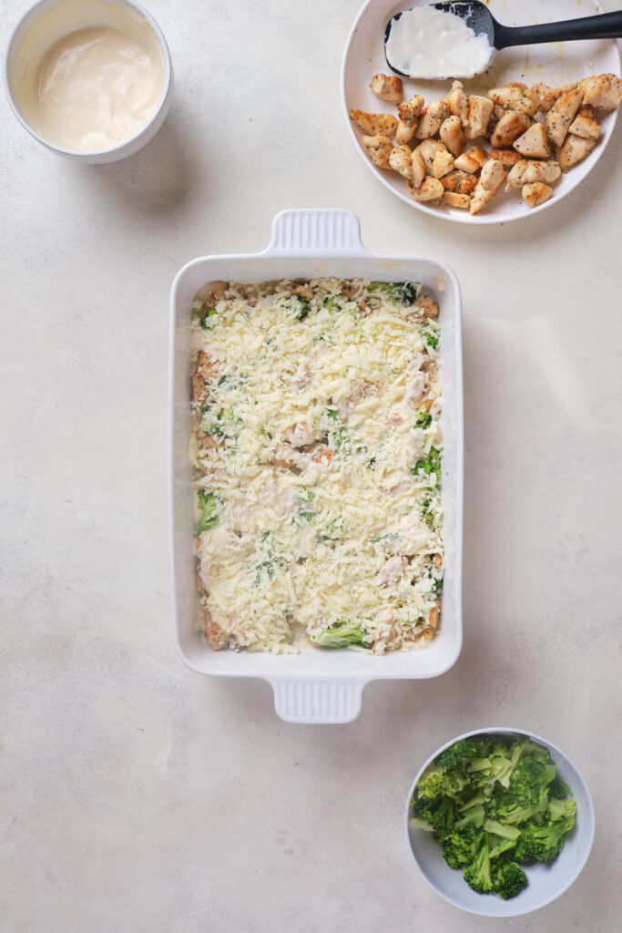 A white rectangular baking dish filled with an uncooked mixture topped with shredded cheese.