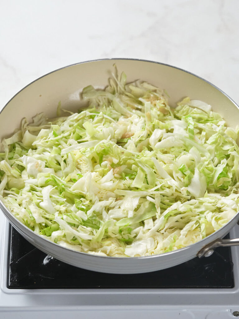 A pan of chopped cabbage being cooked on a stove.