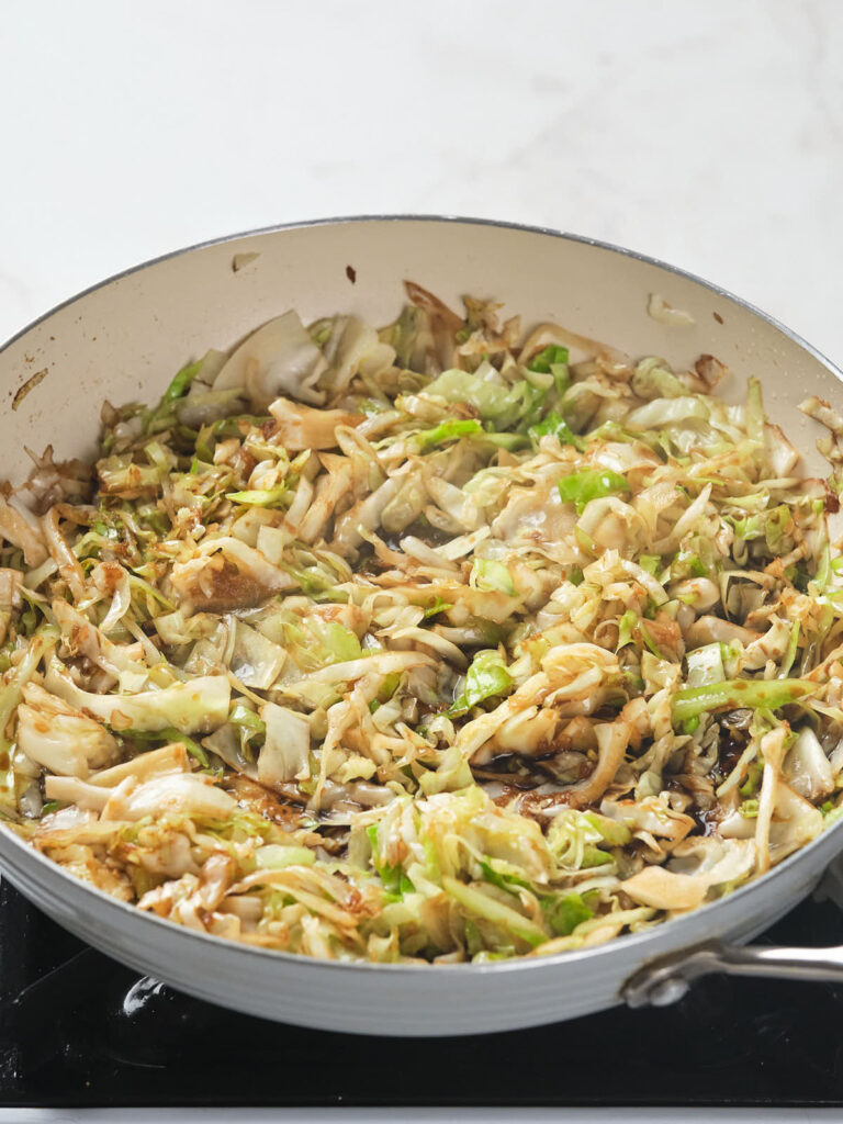 A skillet filled with sautéed cabbage and onions on a stovetop.