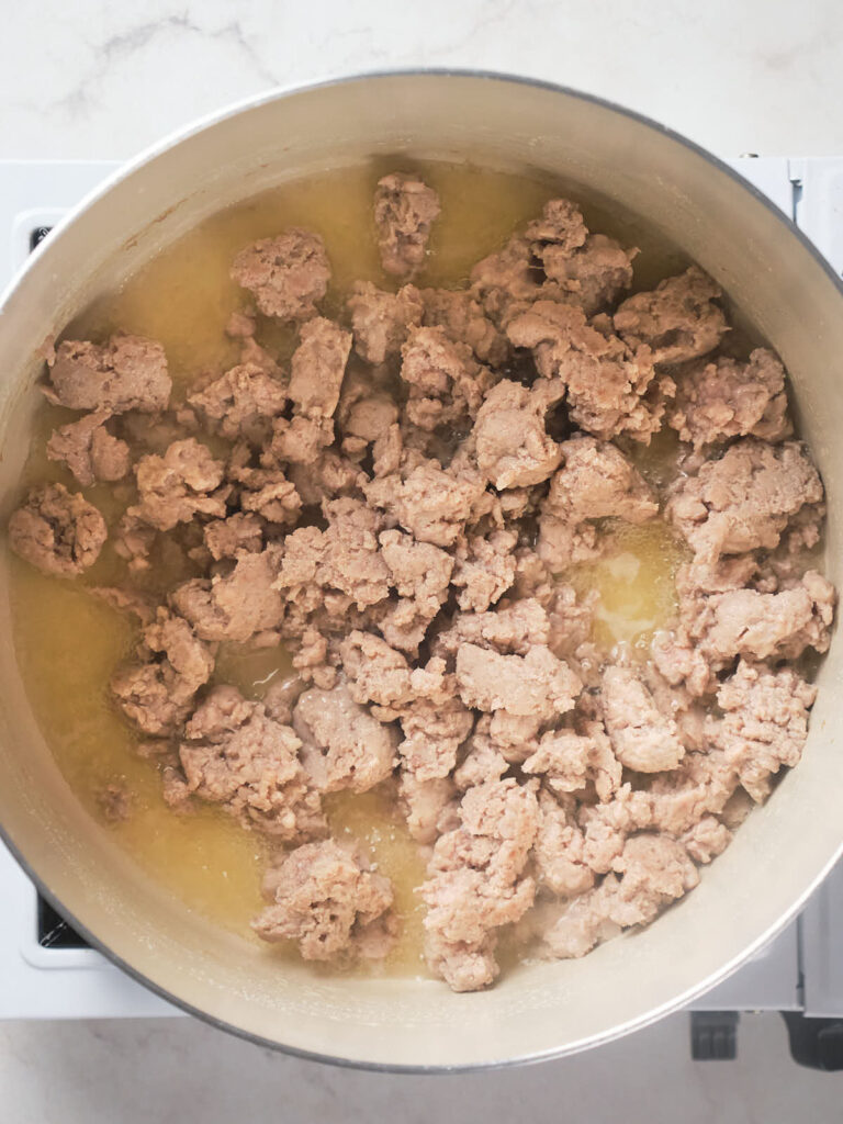 Ground meat being cooked in a large stainless steel pot on a stove.