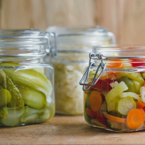 Three glass jars filled with pickled vegetables displayed on a wooden surface.