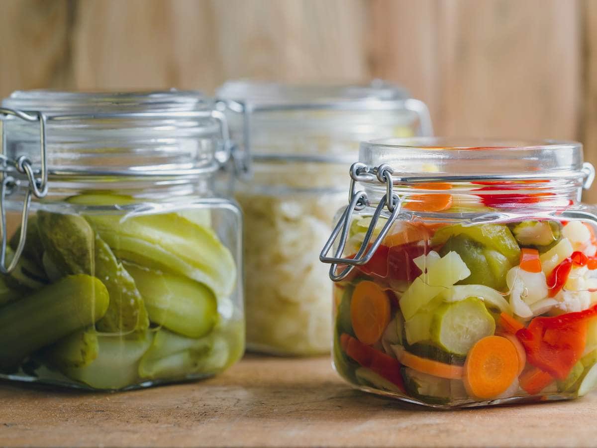 Three glass jars filled with pickled vegetables displayed on a wooden surface.