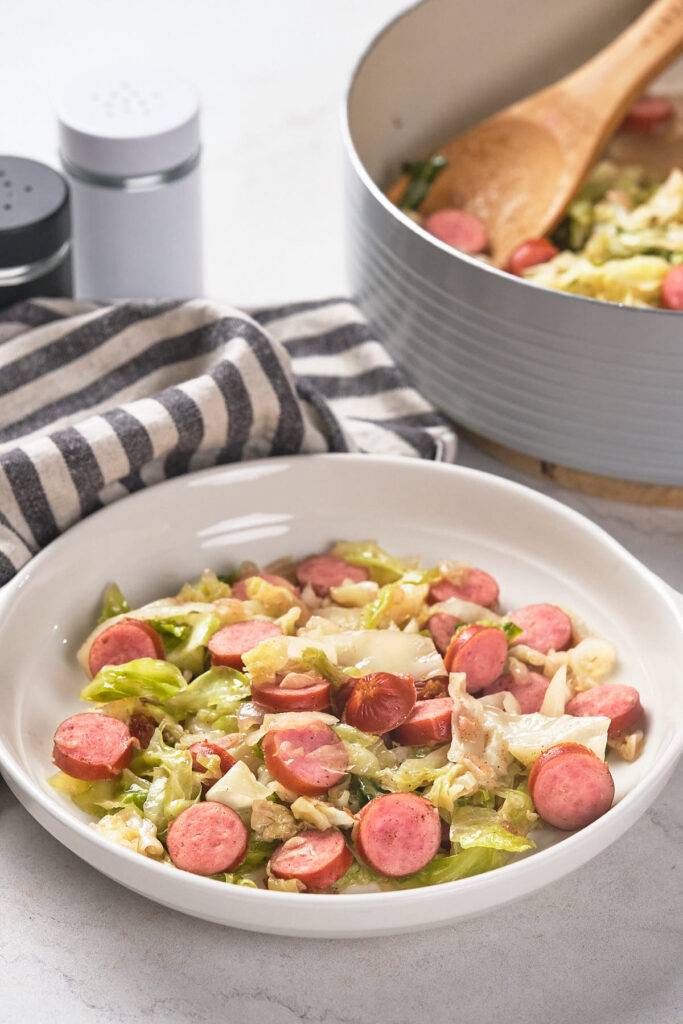 A plate of sautéed cabbage and sliced sausages sits on a table.