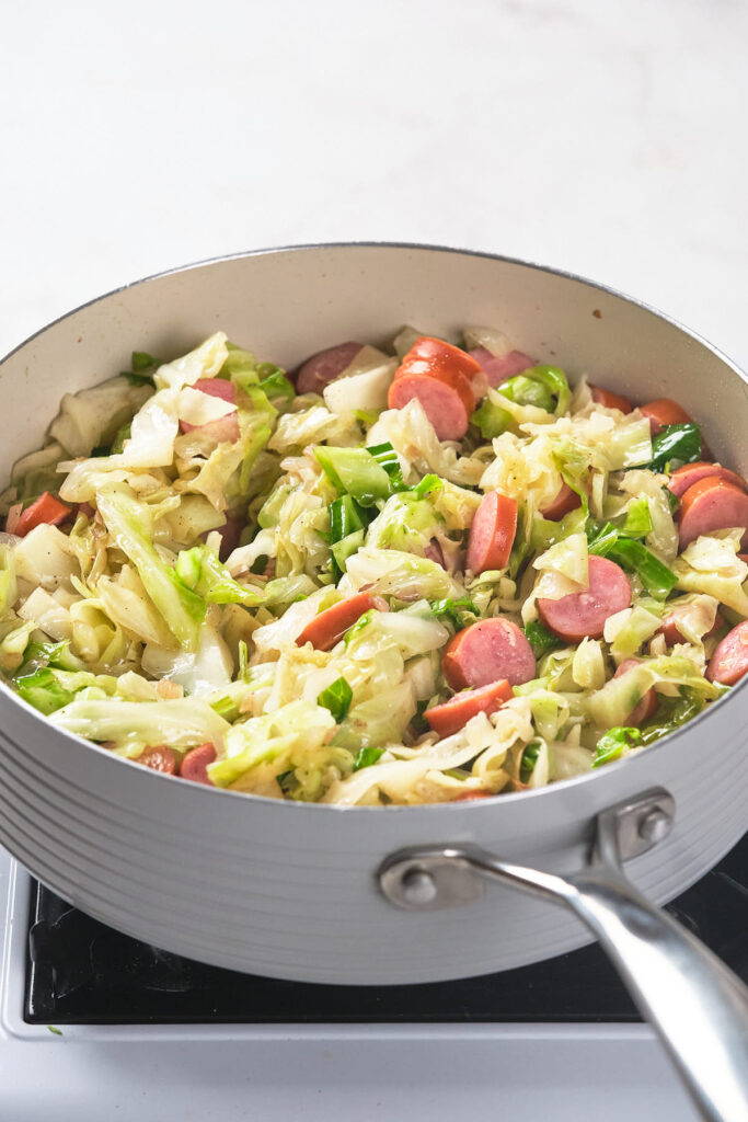 A skillet filled with sautéed cabbage and sliced sausages.