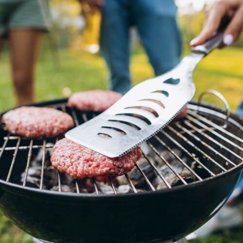 Three people are grilling hamburger patties on a charcoal grill.