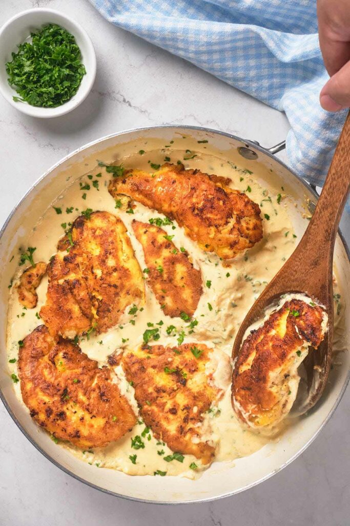 A skillet containing creamy, herb-garnished chicken breasts.