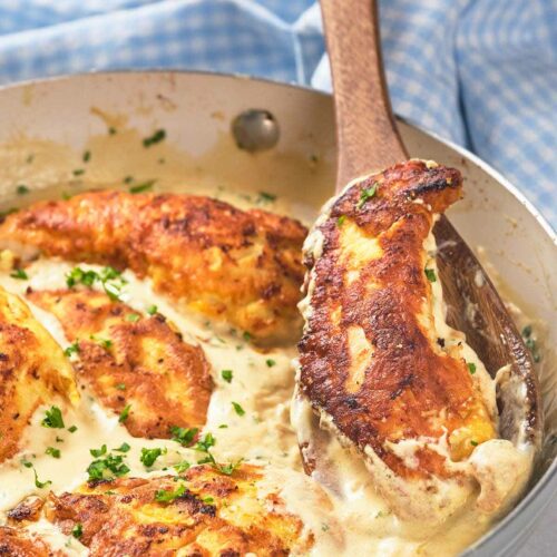 A skillet with creamy garlic chicken being stirred by a wooden spoon.