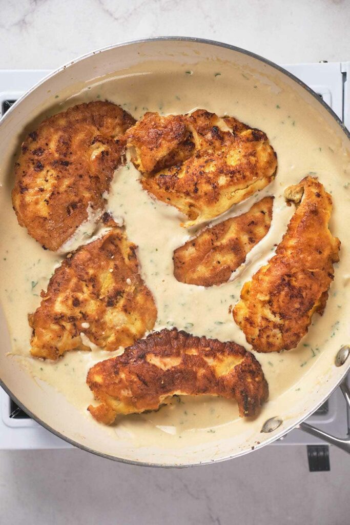 A skillet with cooked healthy chicken francese in sauce.